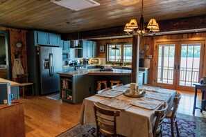 A spacious kitchen with wooden cabinets, a central island, and a dining area with a table set for four. - Private Adirondack Compound! (Saint Regis Falls)