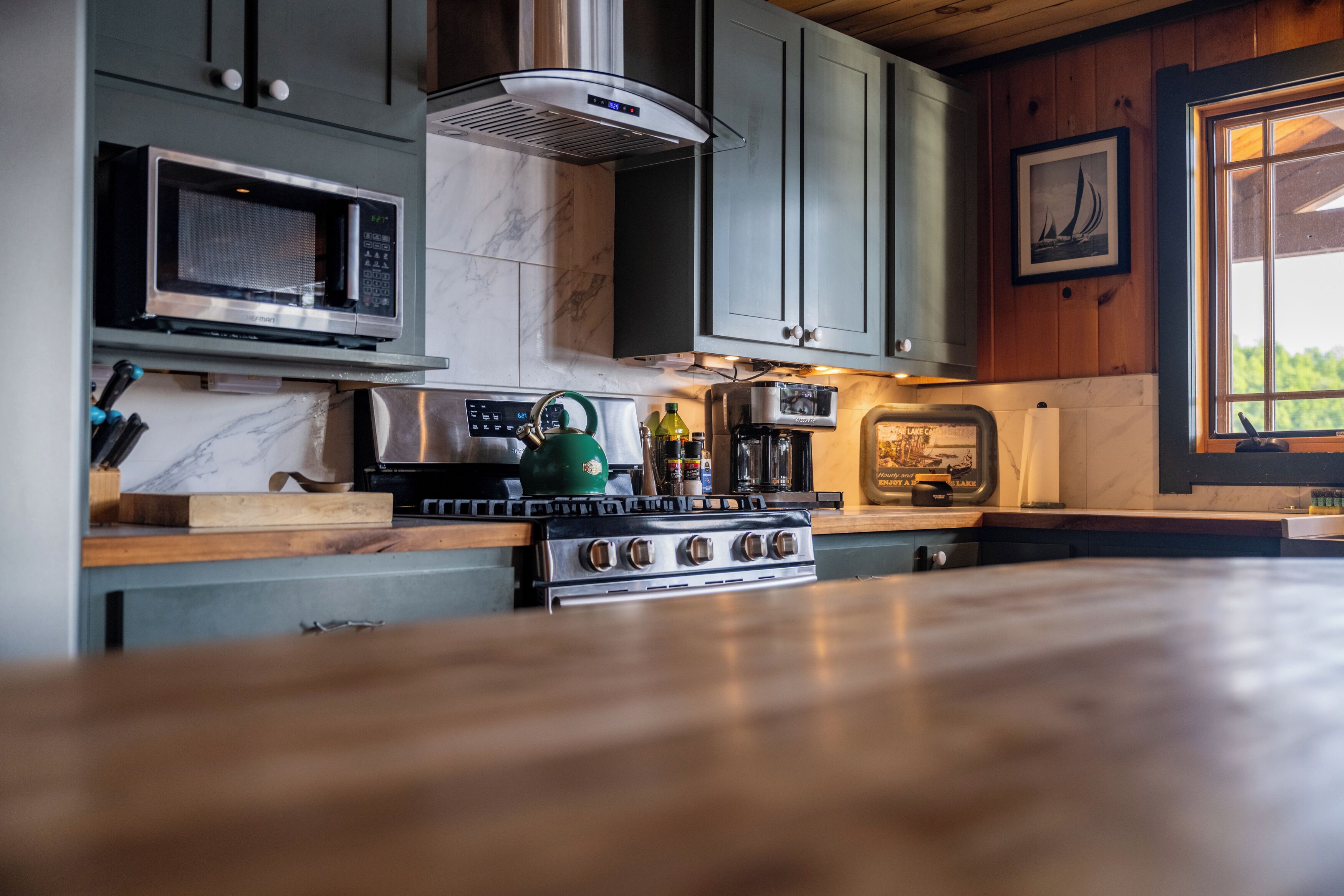 A kitchen with a stainless steel stove, a microwave, and a green kettle.