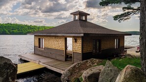 A wooden cabin with a dock, situated by a lake with a forested backdrop. - Private Adirondack Compound! (Saint Regis Falls)
