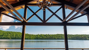 A covered wooden deck with a view of a lake and forest. - Private Adirondack Compound! (Saint Regis Falls)