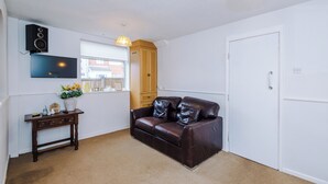 A room with a brown leather sofa, a television mounted on the wall, a wooden cabinet, and a small table with decorative items. - Spacious 3 Bedroom Home in Westhoughton (Westhoughton)