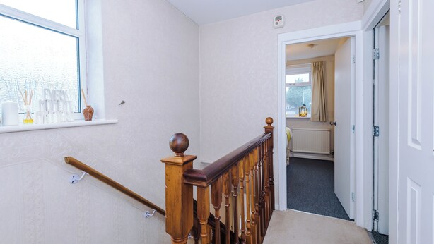 A hallway with a wooden staircase, a radiator, and a door leading to another room. - Spacious 3 Bedroom Home in Westhoughton (Westhoughton)