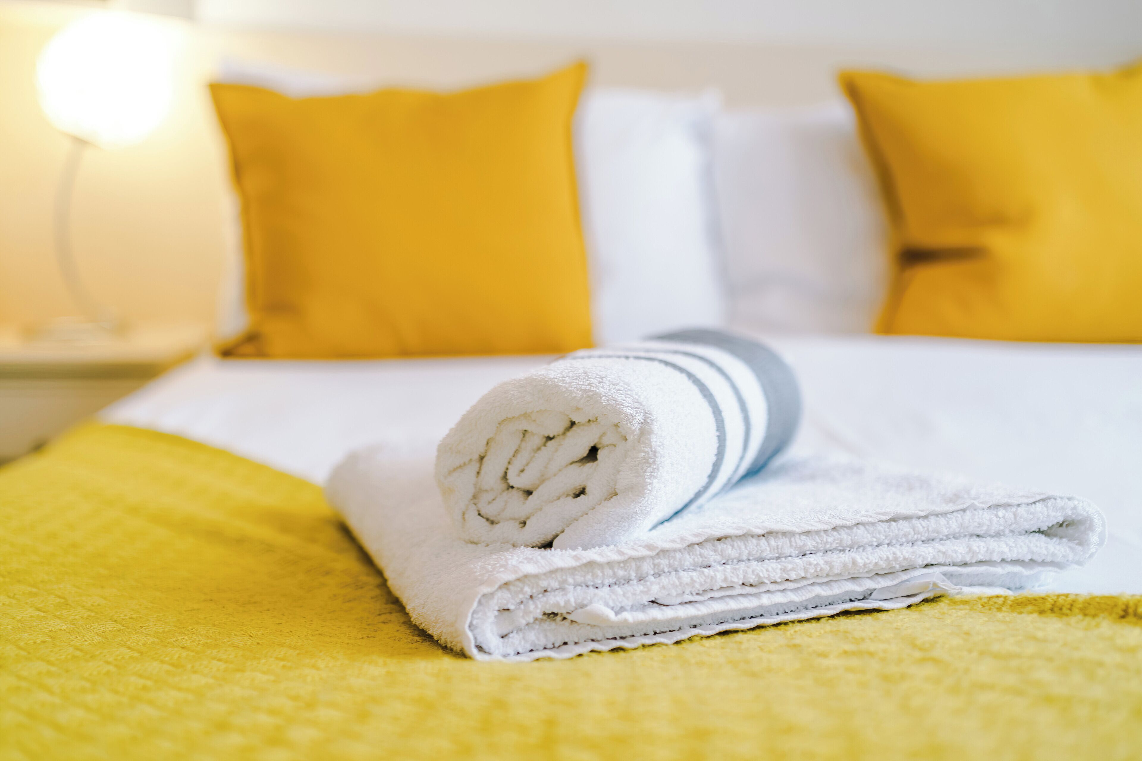 A neatly made bed with a rolled white towel, a yellow blanket, and two yellow pillows.