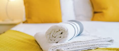 Una cama bien hecha con una toalla blanca enrollada, un edredón amarillo y dos almohadas amarillas.