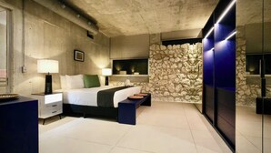 Ein modernes Schlafzimmer mit einer Wand aus Stein, einem großen Bett, Nachttischen und einer Bank.