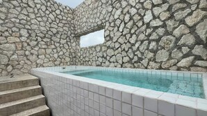 Eine Steinsäule mit einer rechteckigen Öffnung, ein mit Fliesen ausgelegter Pool und Betonstufen, die zu dem Pool führen.