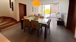 Un espace repas moderne avec une table et des chaises en verre, un escalier et une grande fenêtre donnant sur l’extérieur.