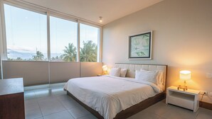 A bedroom with a large bed, a nightstand, a bedside lamp, and a window with blinds. - Oceanfront 2BR at Ultravioleta Cabarete | Fast WiFi, Balcony & Parking (Cabarete)