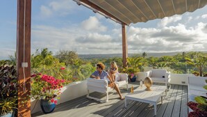 A covered outdoor seating area with white furniture, a wooden deck, and potted plants. - Oceanfront 2BR at Ultravioleta Cabarete | Fast WiFi, Balcony & Parking (Cabarete)