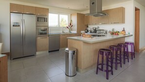 A modern kitchen with stainless steel appliances, wooden cabinets, and a central island with bar stools. - Oceanfront 2BR at Ultravioleta Cabarete | Fast WiFi, Balcony & Parking (Cabarete)
