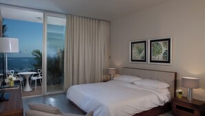 Habitación de hotel con cama, mesitas de noche, una silla, escritorio y vistas al océano.