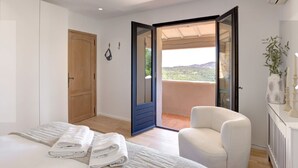 Ein Schlafzimmer mit Bett, einem Sessel, einer Holztür und einem Balkon mit Aussicht.