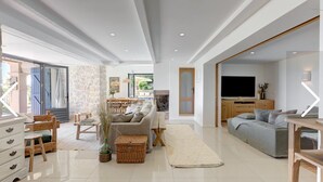 Ein geräumiger Wohnbereich mit einer Couch, einem Esstisch und einem Fernseher. Eine Steinwand und eine Holztür sind ebenfalls vorhanden.