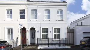 A white two-story building with a red door, a black metal fence, and two parked cars. - Stylish 1-Bed Apartment in Fairview (Cheltenham)