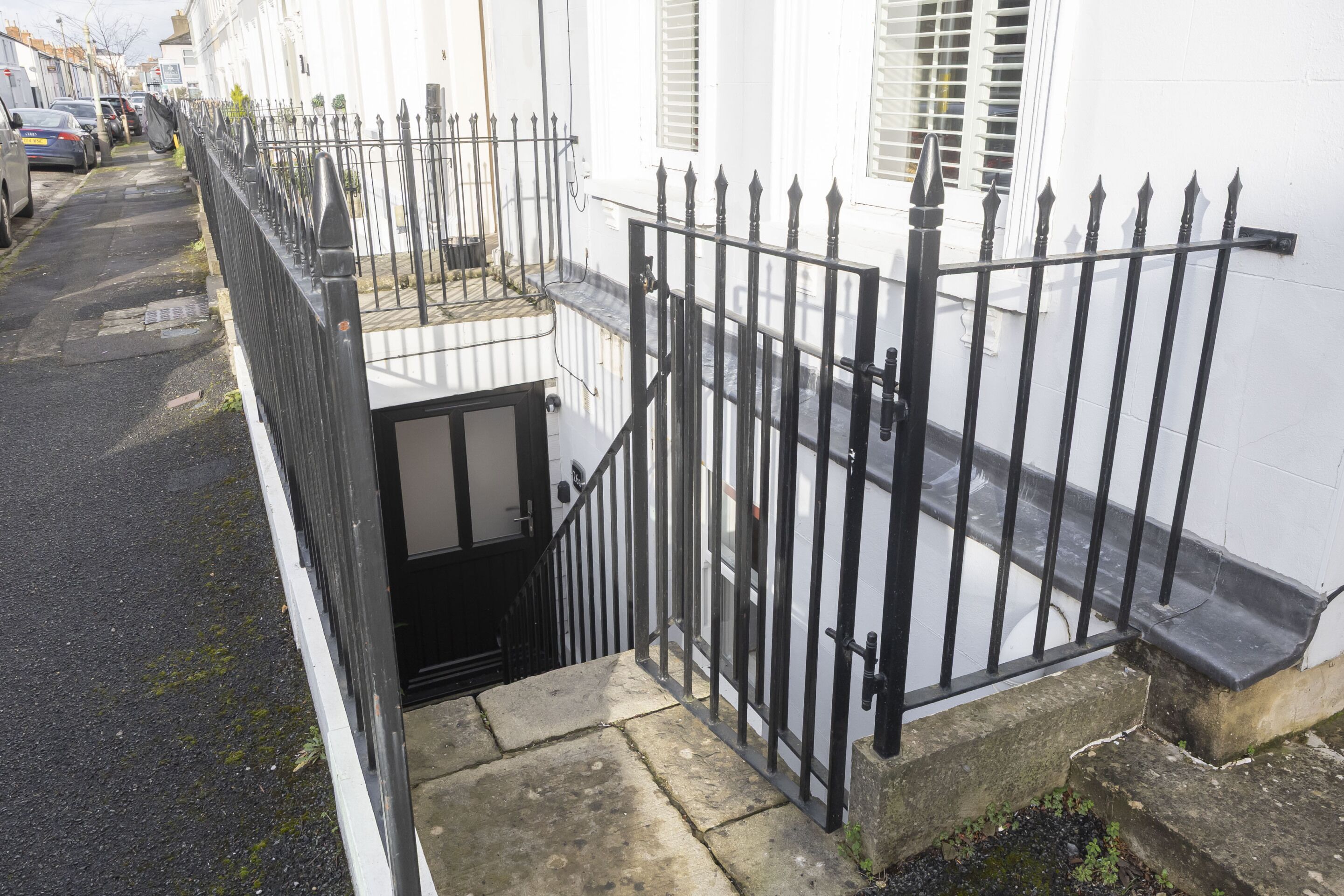 A narrow street with a black metal fence and a white building with a small balcony.