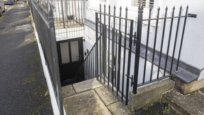 A narrow street with a black metal fence and a white building with a small balcony. - Stylish 1-Bed Apartment in Fairview (Cheltenham)