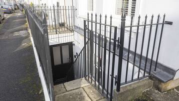 A narrow street with a black metal fence and a white building with a small balcony.