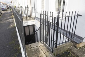 A narrow street with a black metal fence and a white building with a small balcony. - Stylish 1-Bed Apartment in Fairview (Cheltenham)
