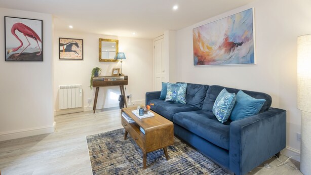 A modern living room with a dark blue sofa, a wooden coffee table, and a large abstract painting. - Stylish 1-Bed Apartment in Fairview (Cheltenham)
