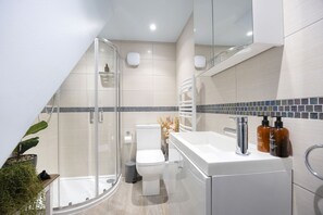 A modern bathroom with a glass shower enclosure, a white toilet, and a vanity with a mirror and two bottles of shampoo. - Stylish 1-Bed Apartment in Fairview (Cheltenham)