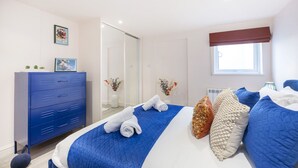 A bedroom with a bed, a blue dresser, a window, and a mirror. - Stylish 1-Bed Apartment in Fairview (Cheltenham)