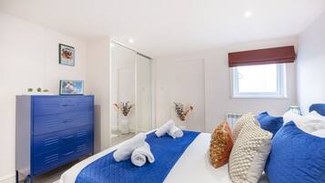 A bedroom with a bed, a blue dresser, a window, and a mirror.
