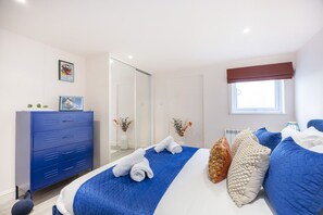 A bedroom with a bed, a blue dresser, a window, and a mirror. - Stylish 1-Bed Apartment in Fairview (Cheltenham)
