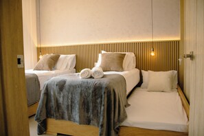 Zwei Einzelbetten mit Holzkopfteilen, eine graue Decke und zusammengerollte Handtücher auf einem Bett.