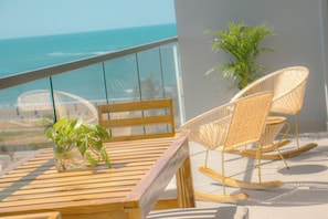 Ein Holztisch mit einem Blumentopf, ein Schaukelstuhl und Blick aufs Meer.