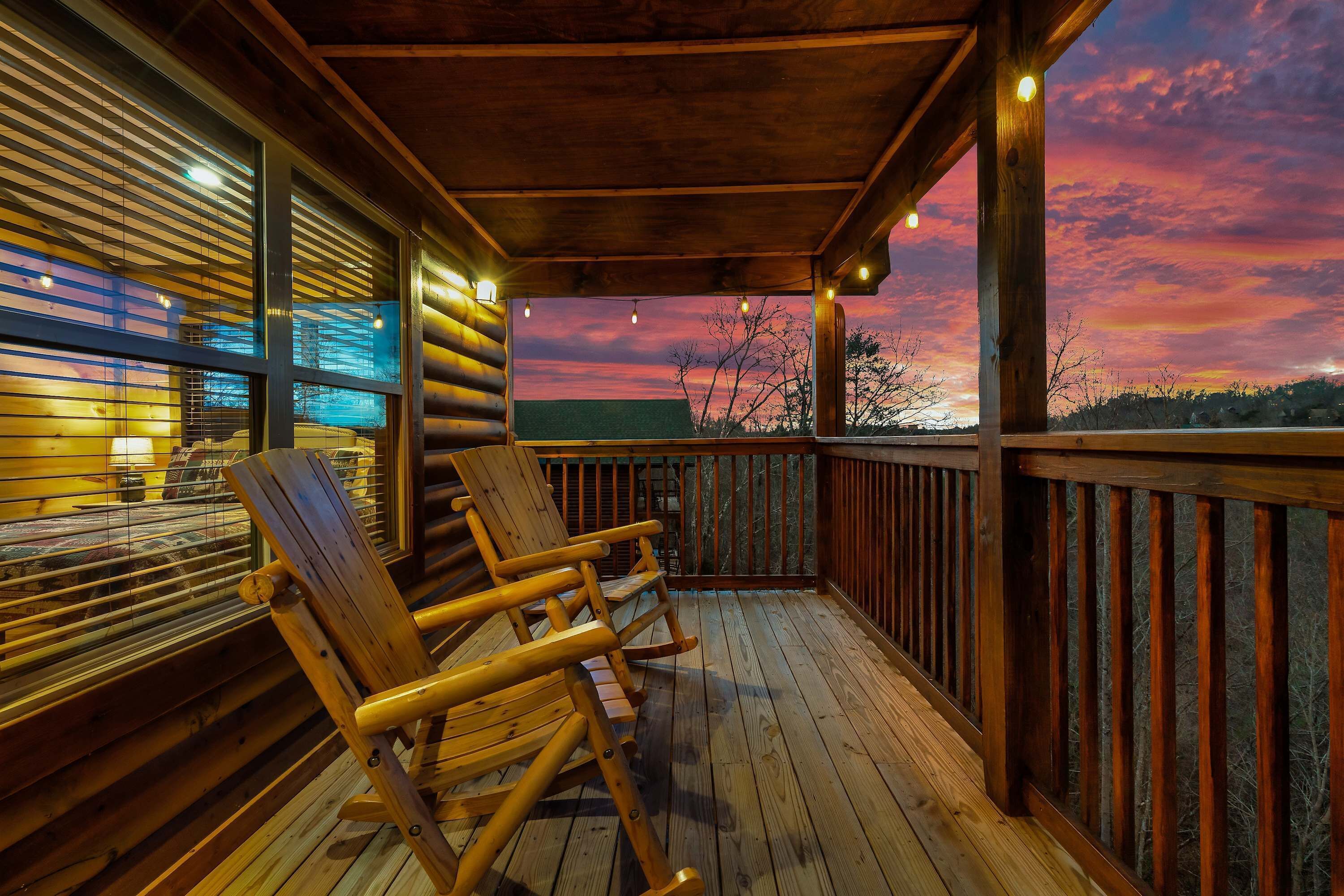 A wooden deck with rocking chairs, a view of the sunset, and a wooden railing.