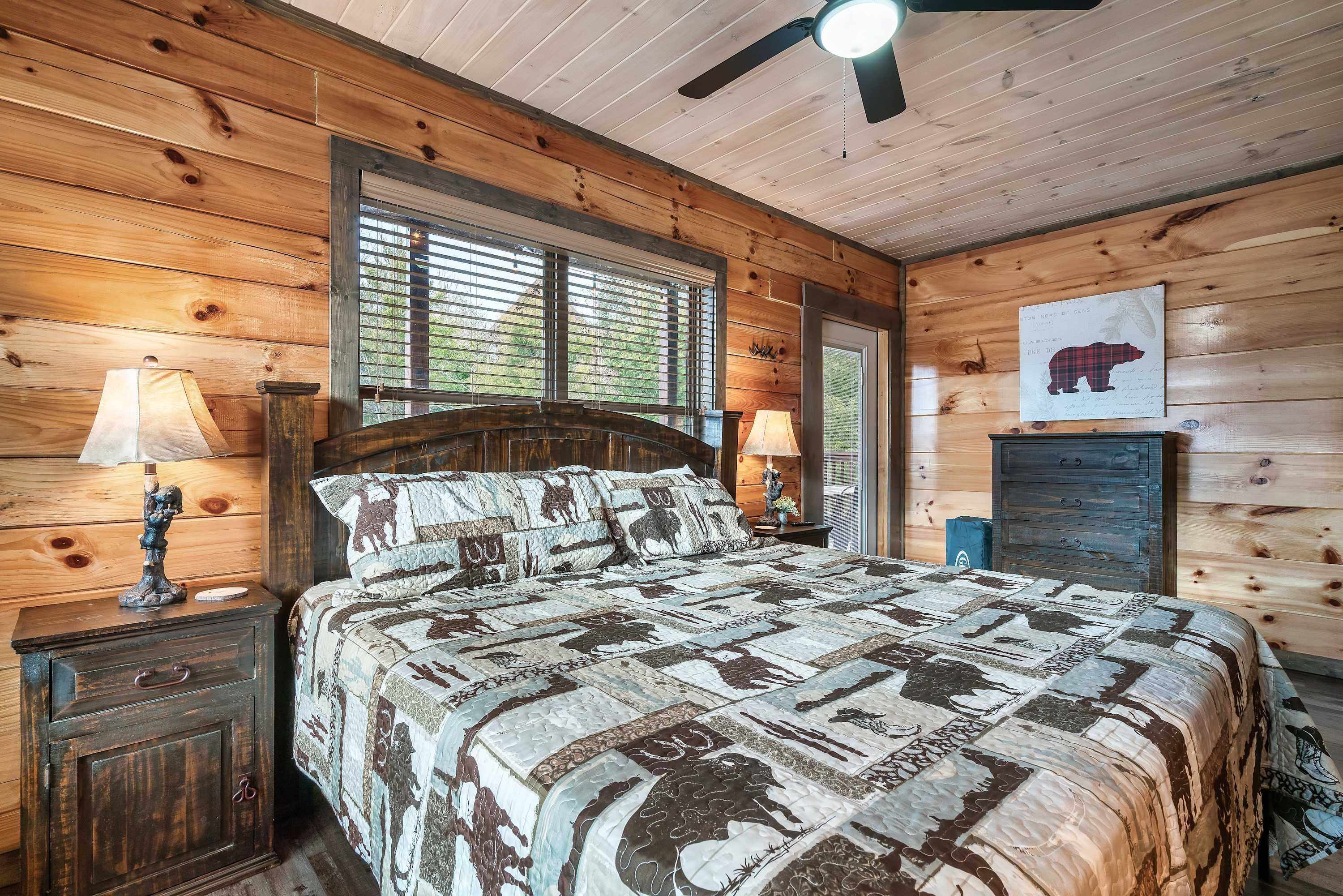 A wooden cabin bedroom with a bed, two nightstands, a ceiling fan, and a window with blinds.