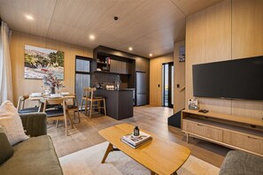 A modern living room with a sofa, coffee table, and a TV on a stand. - Cosy Peak Retreat with Remarkable Mountain View (Queenstown)
