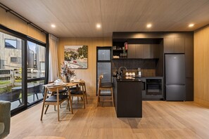 A modern kitchen with a central island, wooden flooring, and large windows offering a view of the outdoors. - Cosy Peak Retreat with Remarkable Mountain View (Queenstown)