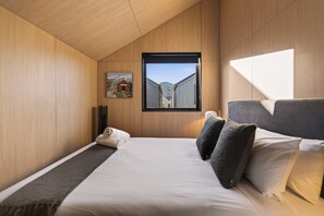 A modern hotel room with a bed, a view of a building through a window, and a painting on the wall. - Cosy Peak Retreat with Remarkable Mountain View (Queenstown)