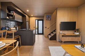 A modern kitchen with a central island, a dining area with wooden furniture, a built-in TV, and a staircase leading to another level. - Cosy Peak Retreat with Remarkable Mountain View (Queenstown)