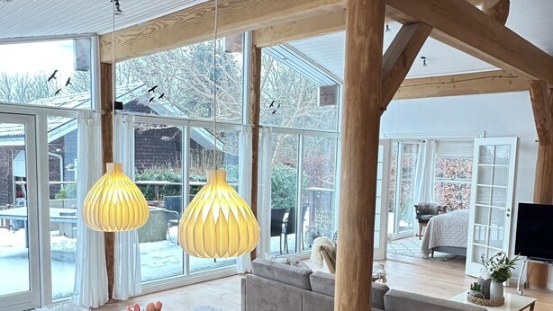 A spacious room with a large dining table, wooden beams, and large windows offering a view of the outdoors. - Spacious holiday home near beach and nature (Jægerspris)