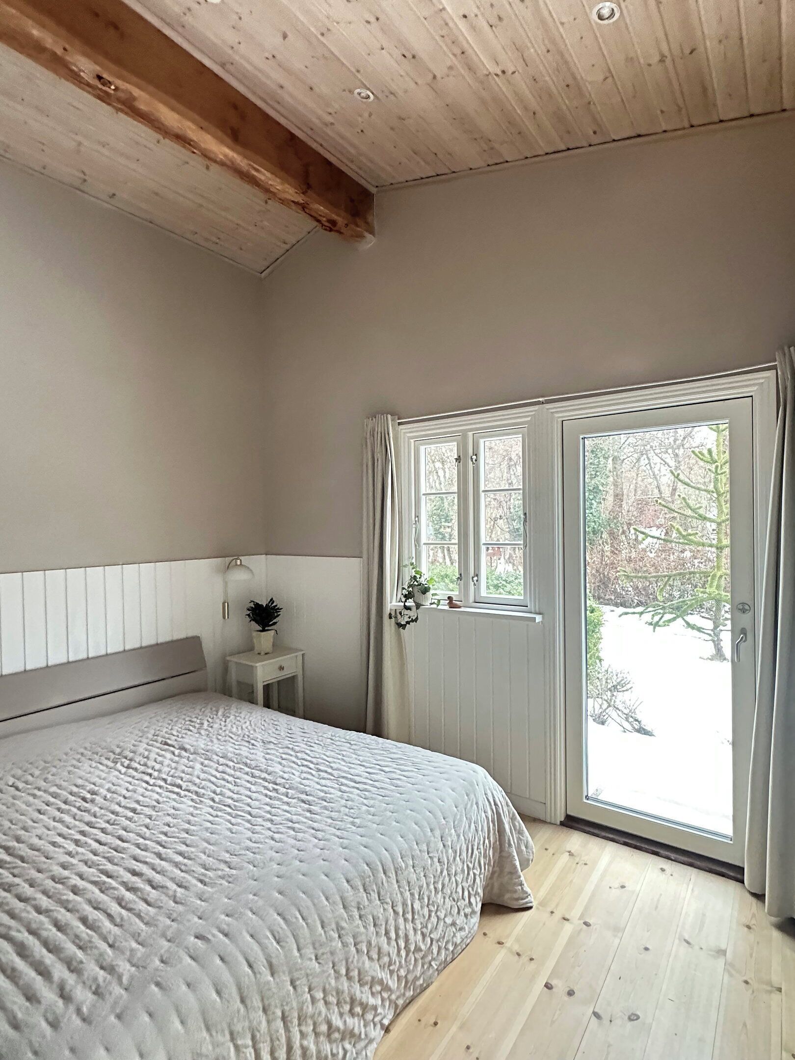 Ein Schlafzimmer mit Bett, Nachttisch, Fenster mit Vorhängen und Blick ins Freie.