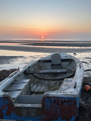 Een klein bootje op het strand, met een zonsondergang op de achtergrond.