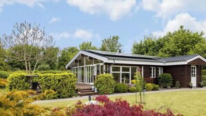 A two-story house with a covered porch, surrounded by well-maintained gardens and trees. - Spacious holiday home near beach and nature (Jægerspris)