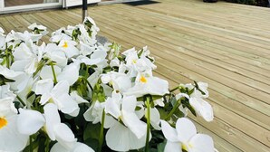 A modern house with large glass doors, a wooden deck, and white flowers in the foreground. - Spacious holiday home near beach and nature (Jægerspris)