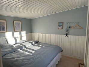 A bedroom with a bed, a headboard, a wall-mounted coat rack, and framed pictures.