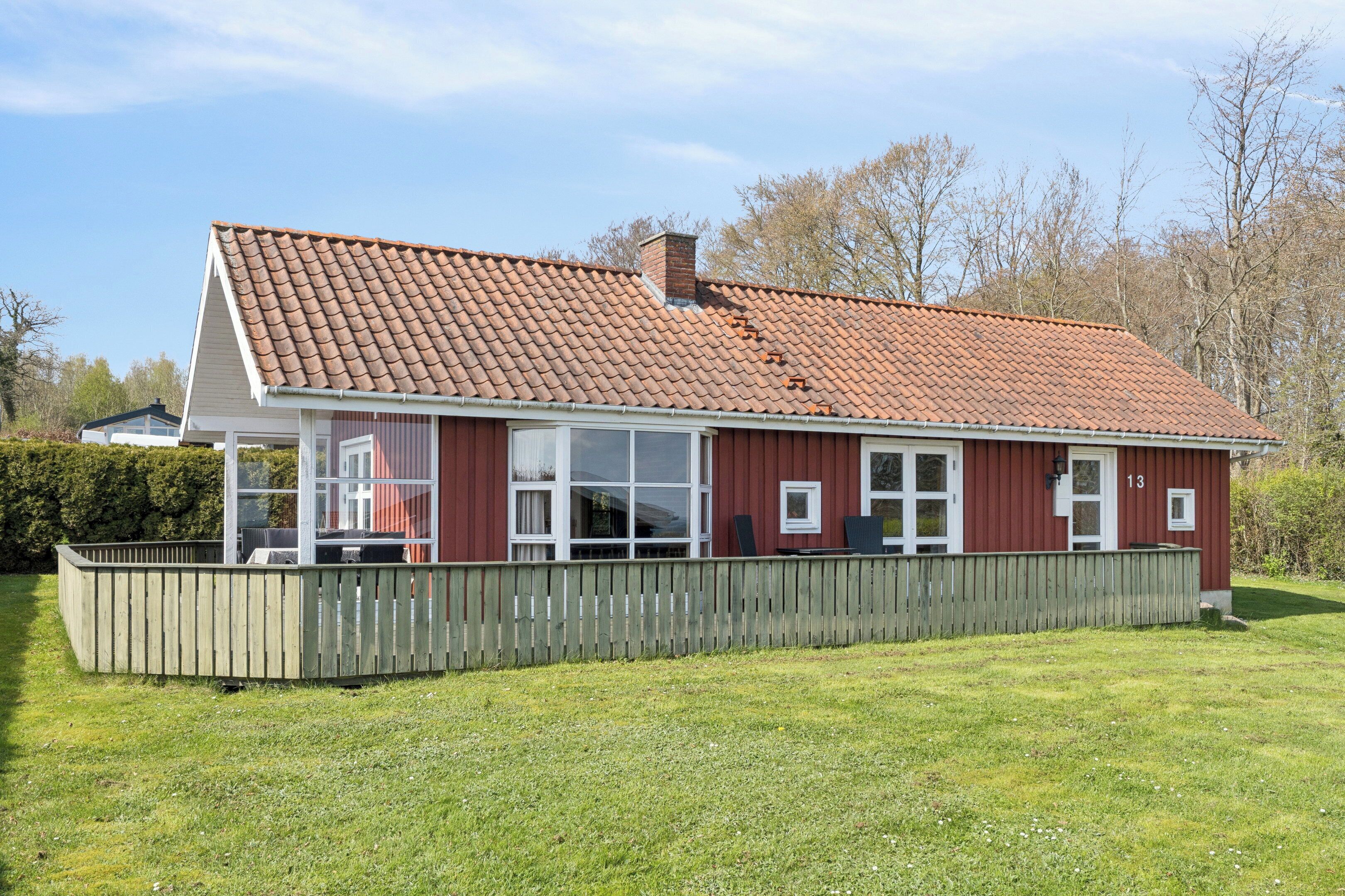 Een rode woning met pannendak, houten omheining en een gazon.