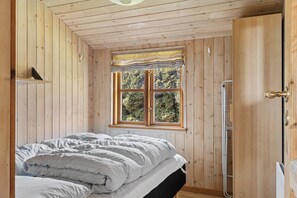 Una stanza con rivestimento in legno, un letto, una finestra vista alberi e una porta.