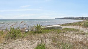 Un paisaje costero con una playa arenosa, una barrera de hormigón y una costa distante con edificios.