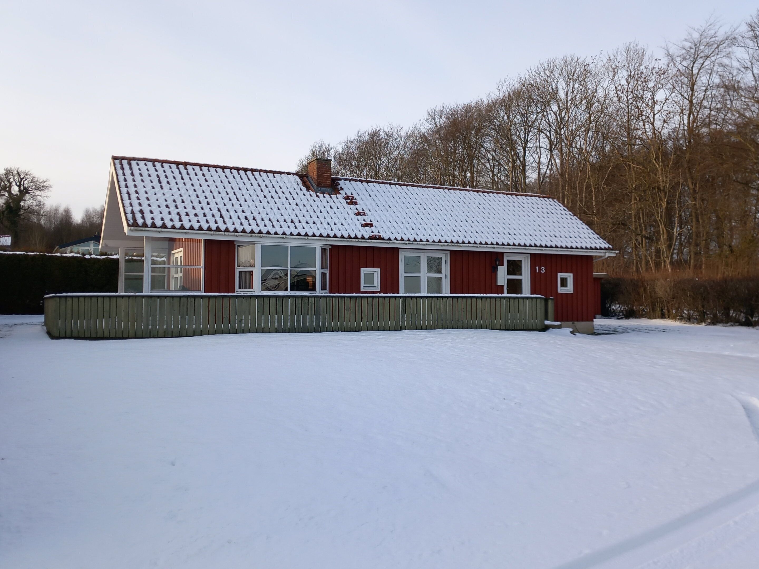 A red building with a snow-covered roof and a fenced yard.