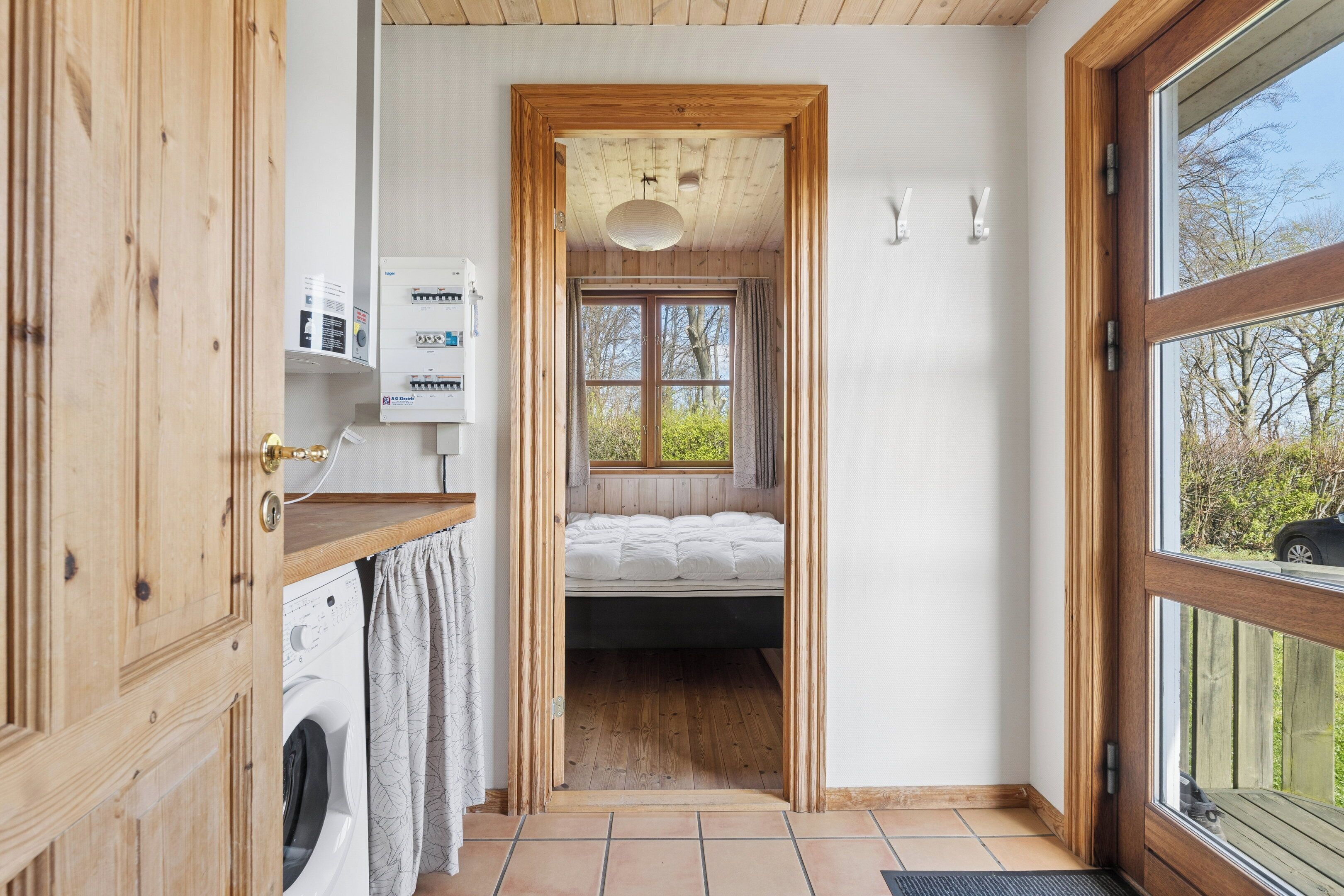 A compact room with a bed, a washing machine, and a window with a view of trees.
