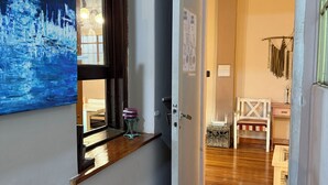 Un pasillo con piso de madera, una puerta que da a una habitación con una cama y una silla, y un cuadro en la pared.