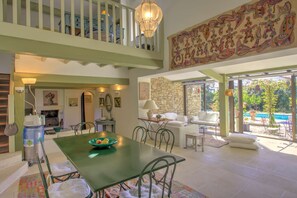A spacious living area with a dining table, chairs, a sofa, and a view of an outdoor swimming pool. - La Garrigue de Gordes (Gordes)