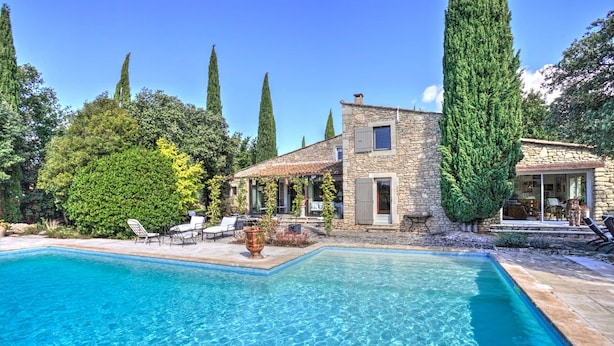 A stone house with a swimming pool, surrounded by tall trees and a clear blue sky. - La Garrigue de Gordes (Gordes)