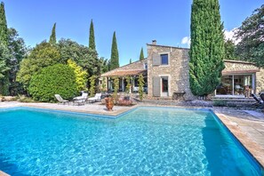 A stone house with a swimming pool, surrounded by tall trees and a clear blue sky. - La Garrigue de Gordes (Gordes)